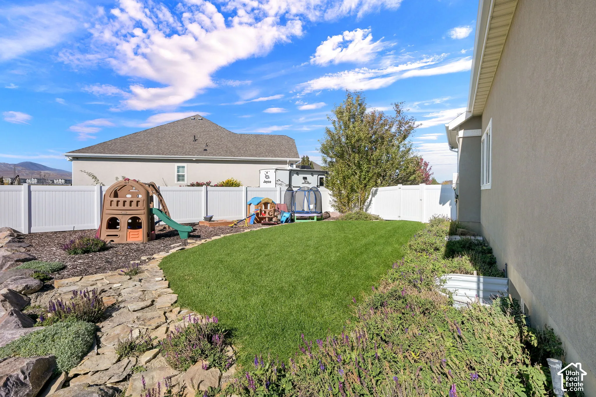 Backyard featuring a manicured lawn, stone pathway, white vinyl fencing, and rock-lined landscaping