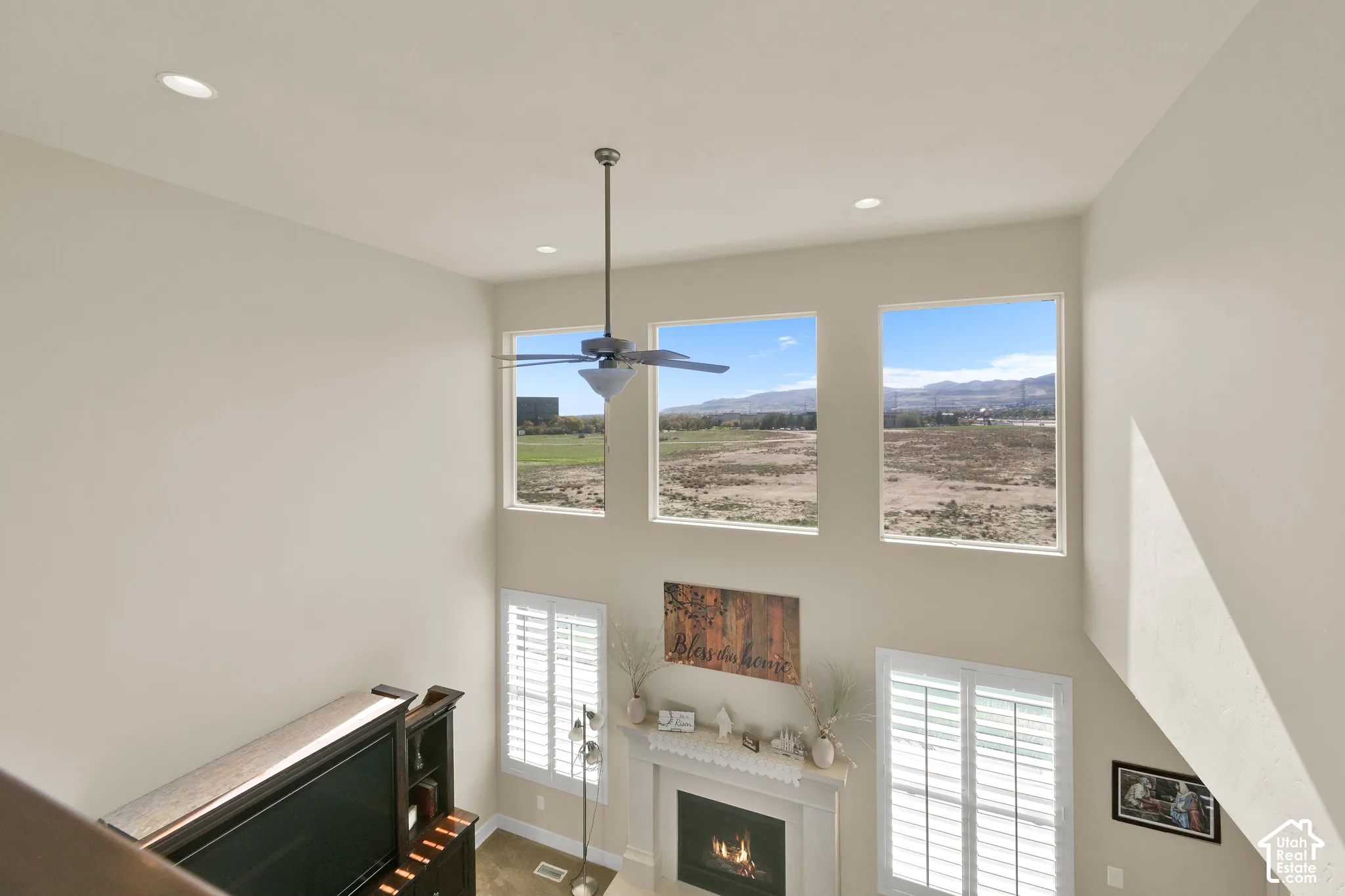 High ceilings featuring recessed lighting, a ceiling fan, and large windows with mountain scenery, paired with a fireplace featuring a detailed mantel