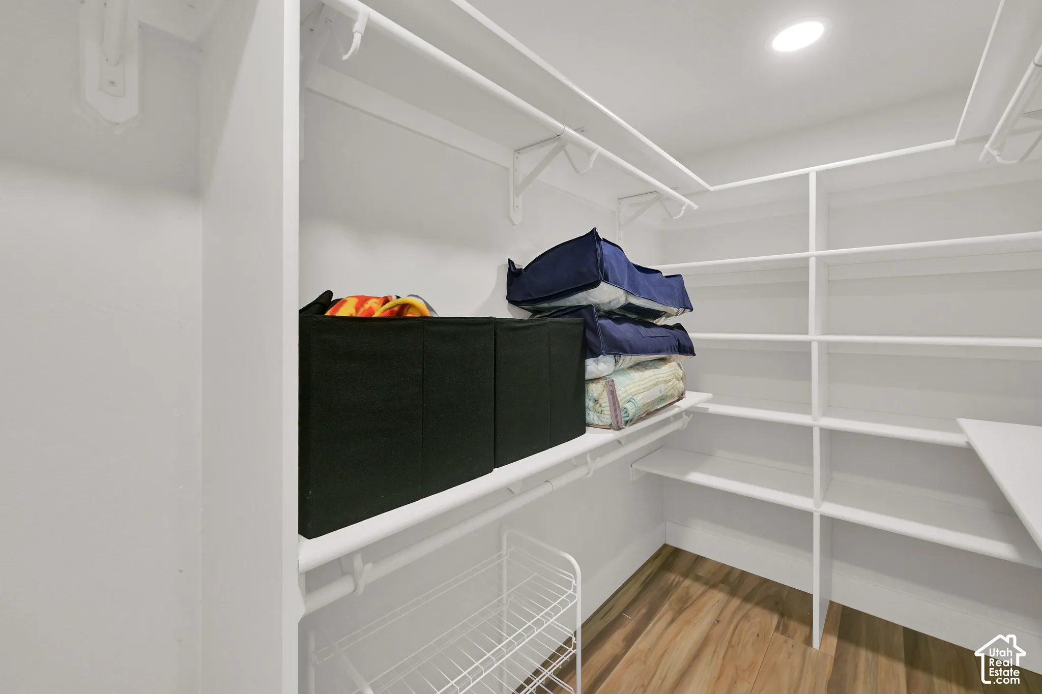 Walk-in closet featuring white multi-tier shelving, integrated clothing rods, and wood-finish flooring