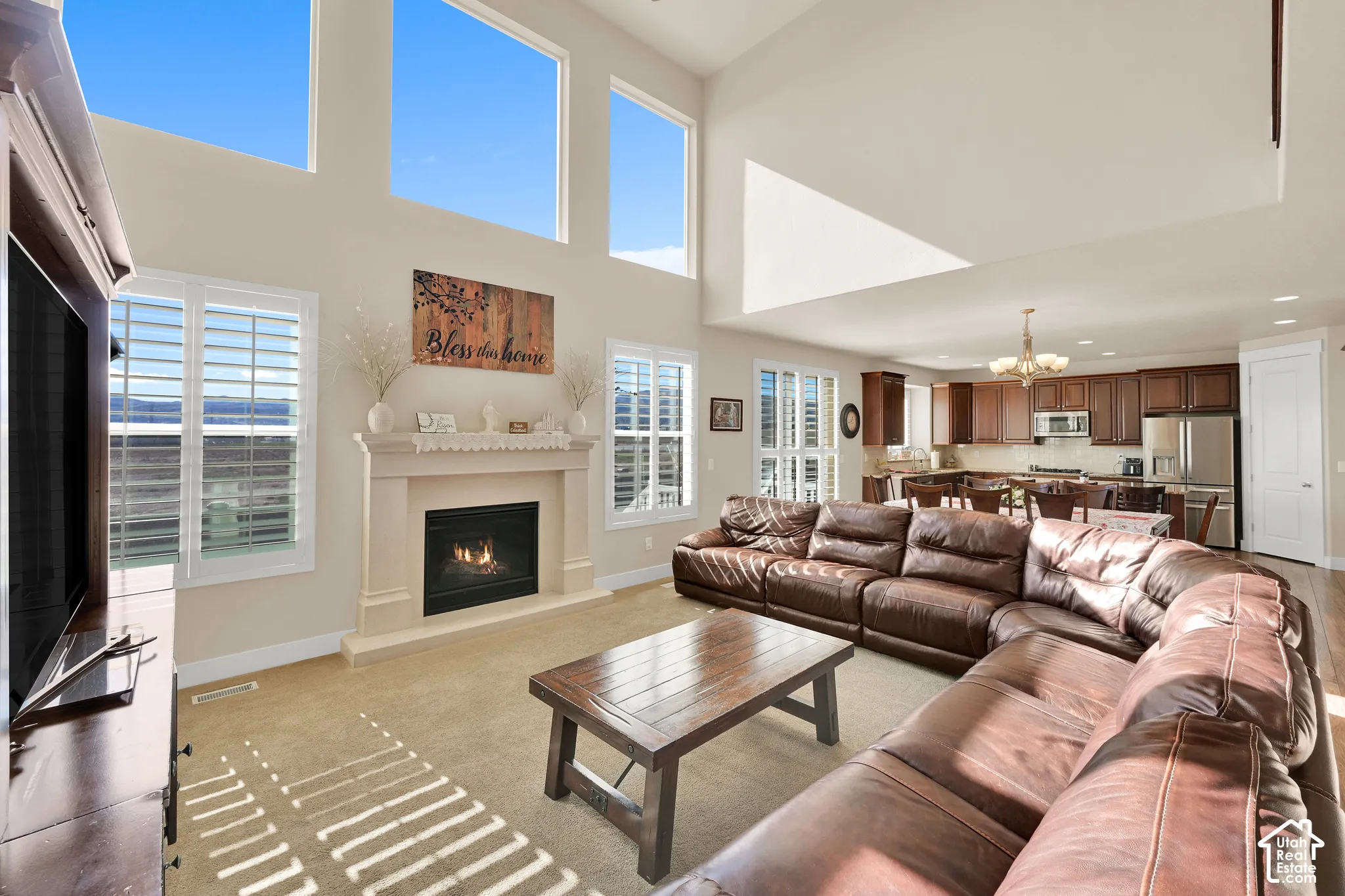 Two-story living area featuring vaulted ceilings, oversized windows, stone-surround fireplace, and plantation shutters