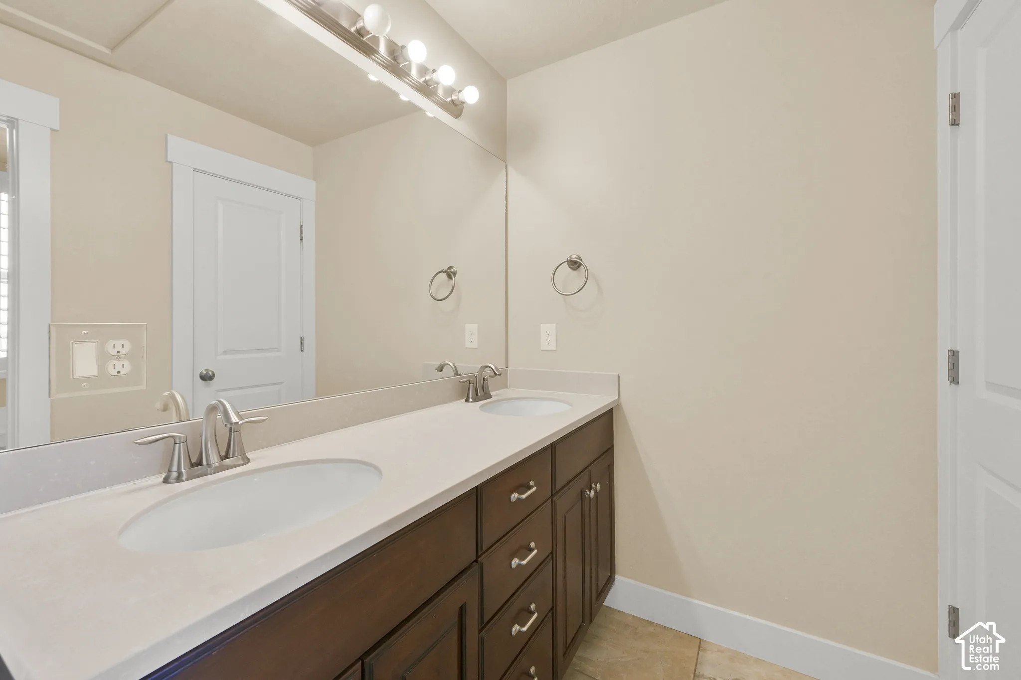 Dual-sink vanity with a solid-surface countertop, dark wood-finish cabinetry, brushed nickel fixtures, and a full-width wall mirror