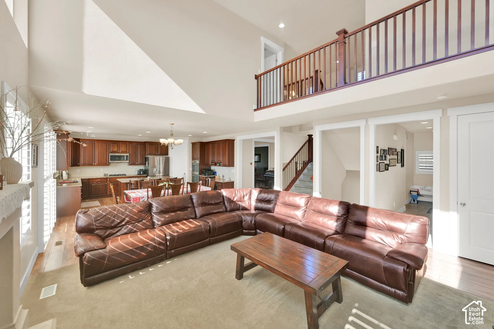 Open-concept floor plan featuring soaring vaulted ceilings, a mezzanine balcony with wood-railing balusters, and a kitchen equipped with built-in cabinetry and stainless steel appliances