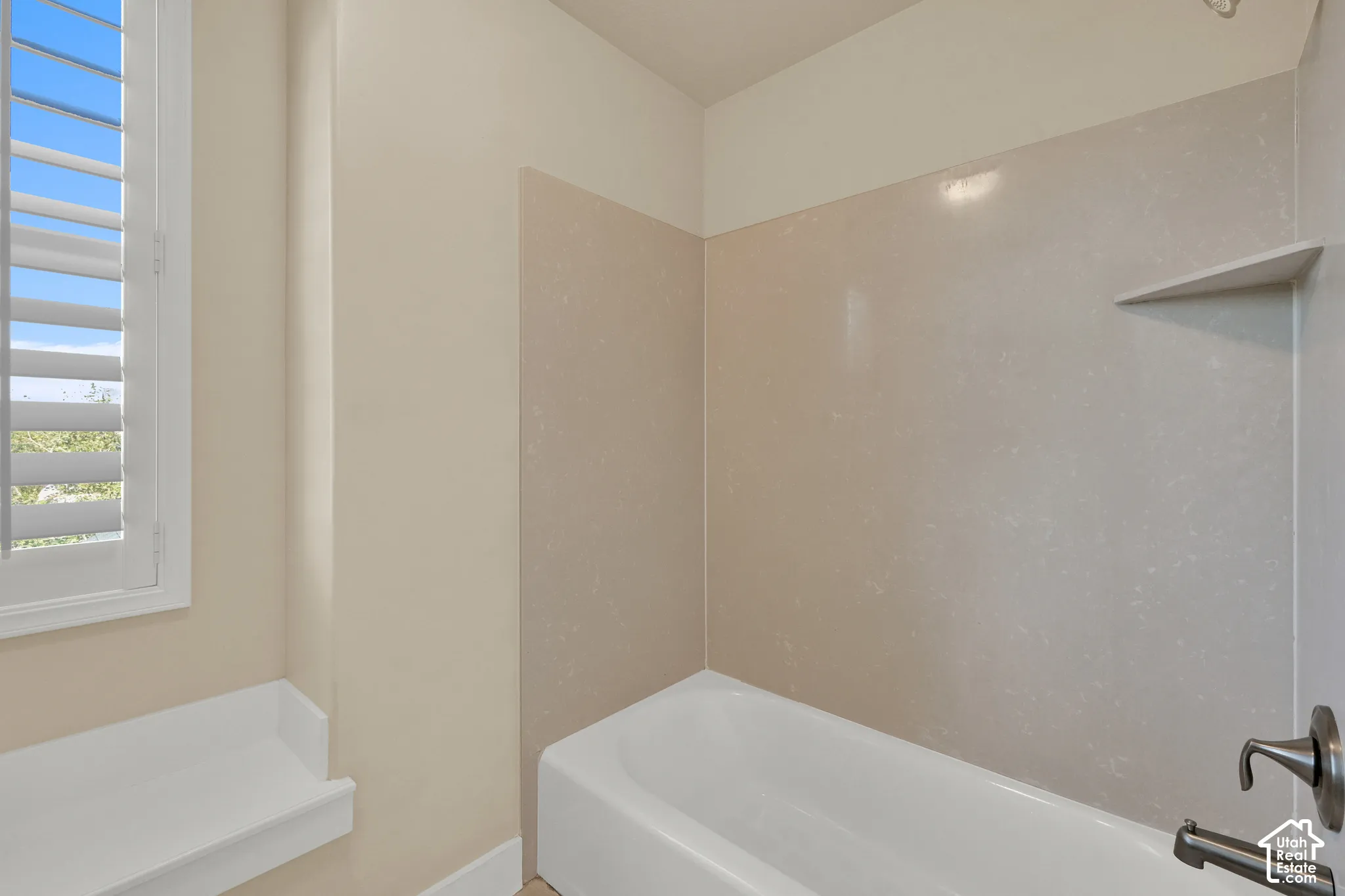 Bathtub with solid-surface surround, integrated shelving, adjustable metal faucet fixture, and window with interior shutters