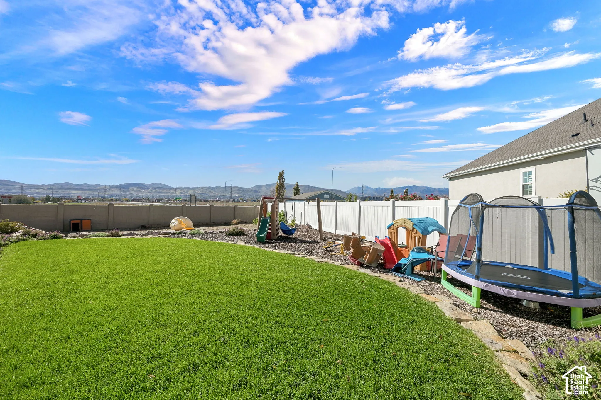 Fenced backyard featuring a manicured lawn, stone hardscaping border, and mountain backdrop