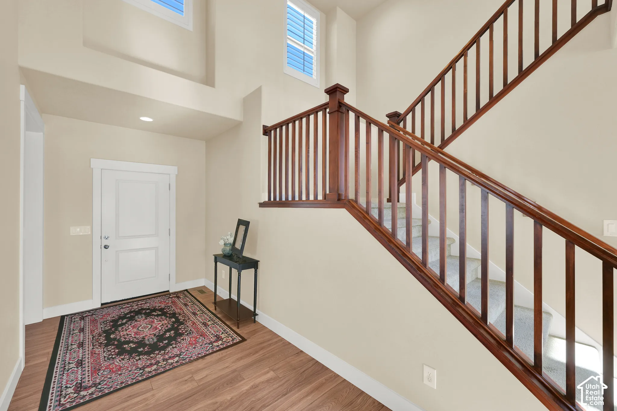 Entryway featuring wood-finish flooring, two-story ceiling, high-reaching windows, and a staircase with stained wood handrails and balusters