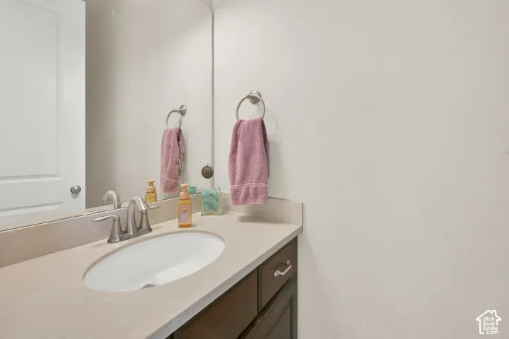 Vanity featuring a stone-composite countertop, undermount oval basin, brushed nickel faucet, wood-finish cabinetry, and full-length wall mirror