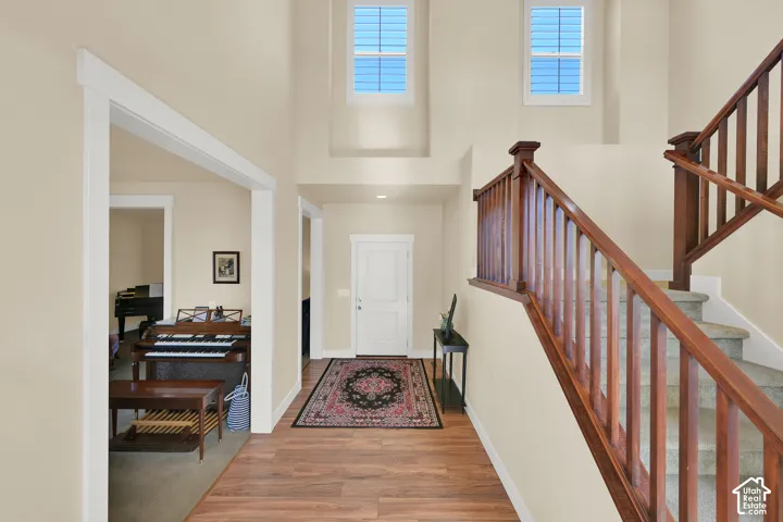 Double-height foyer featuring wood-finish flooring, staircase with a wood railing, and dual transom-style windows