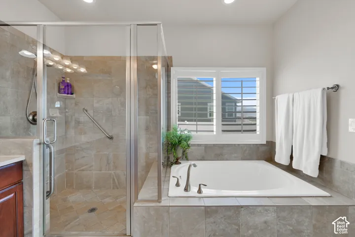 Walk-in shower with glass enclosure and tile surround, deep soaking tub with tile deck, and interior window shutters