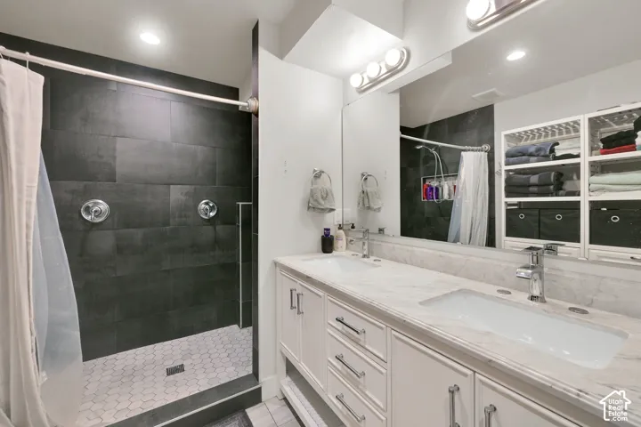 Double-vanity bathroom featuring large-format dark tile shower surrounds, white cabinetry with stone-finish countertops, undermount sinks, and full-width vanity mirrors