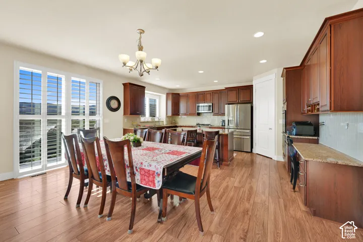 Kitchen featuring custom wood cabinetry, stone countertops, stainless steel appliances, wood-finish flooring, and multi-panel plantation shutters