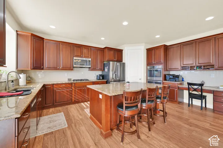 Kitchen featuring wood cabinetry, stone countertops, stainless steel appliances, a center island with bar seating, and wood-finish flooring