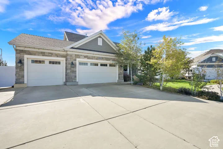 Exterior facade featuring a combination of stone veneer and horizontal siding, a two-car garage, concrete driveway, and mature landscaping
