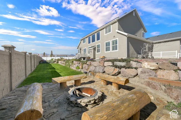 Backyard featuring a stone-paved fire pit, tiered landscaping with natural boulder retaining walls, a level lawn, and a perimeter masonry wall