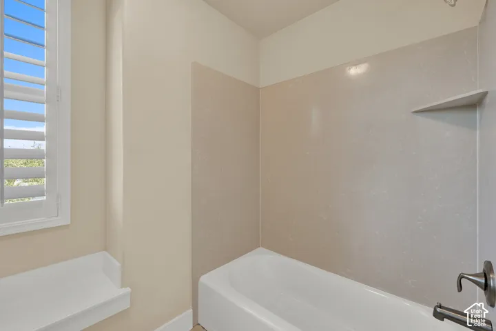 Bathtub with solid-surface surround, integrated shelving, adjustable metal faucet fixture, and window with interior shutters