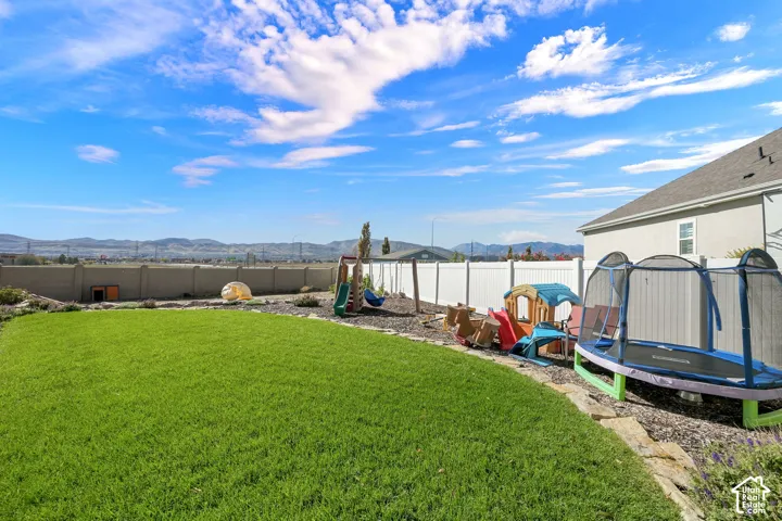 Fenced backyard featuring a manicured lawn, stone hardscaping border, and mountain backdrop