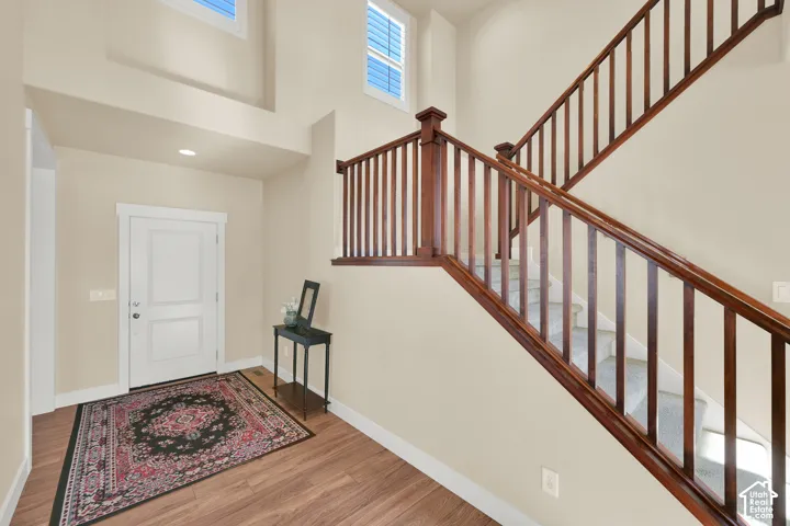 Entryway featuring wood-finish flooring, two-story ceiling, high-reaching windows, and a staircase with stained wood handrails and balusters