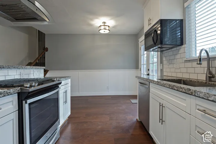 Kitchen featuring white shaker-style cabinetry, stone-patterned countertops, subway tile backsplash, stainless steel appliances, and wood-finish flooring