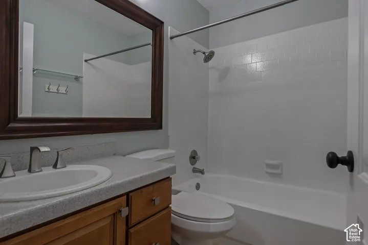 Bathroom featuring a vanity with a stone-finish countertop, an oval under-mount sink, a framed mirror, and a tub-shower combination with tile-surround walls