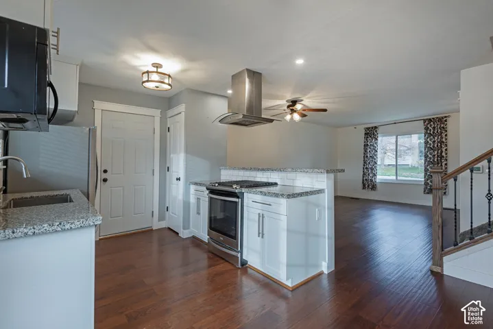 Kitchen featuring white cabinetry, stone-finish countertops, stainless steel range with overhead vent hood, wood-finish flooring, and staircase with wooden handrail