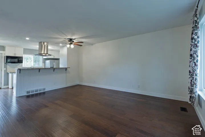 Wood-finish flooring, kitchen peninsula with beadboard detailing, stainless steel chimney-style range hood, and ceiling-mounted fan with integrated light fixture