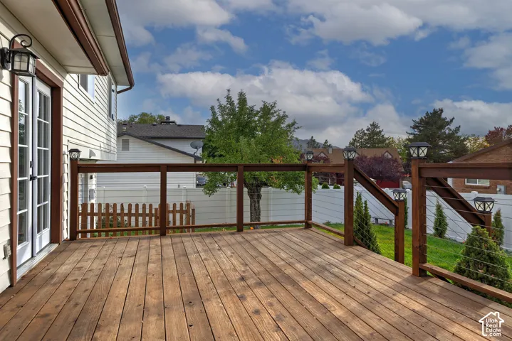 Raised wood deck featuring a railing with integrated cable balusters, post-mounted lighting fixtures, and direct access through French doors