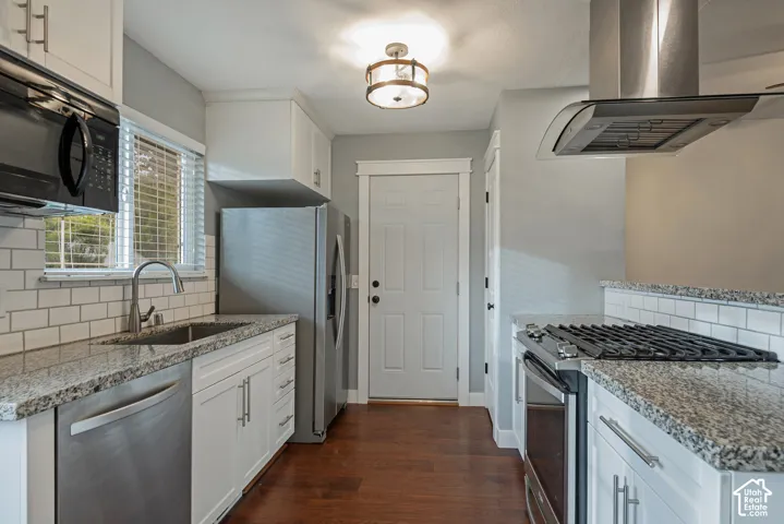 Kitchen featuring white shaker-style cabinetry, stone countertops, subway tile backsplash, stainless steel appliances, and wood-finish flooring