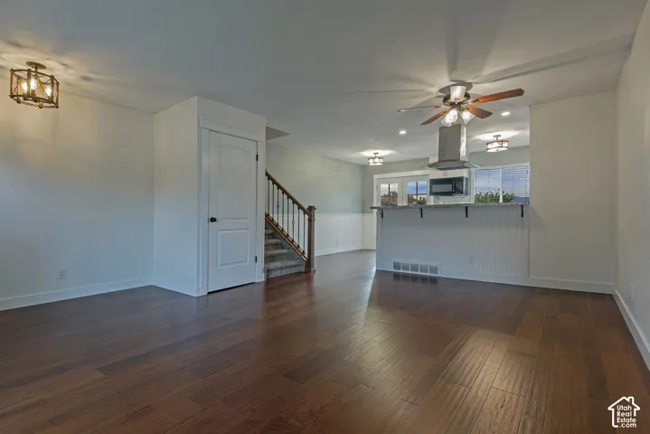 Open-concept space featuring dark wood-finish flooring, a kitchen peninsula with beadboard detailing, recessed lighting, and a staircase with a wooden handrail