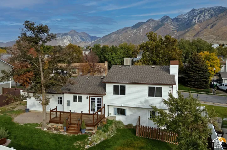 Exterior featuring white horizontal siding, an elevated wood deck, a rear lawn with mature trees, and a mountain backdrop