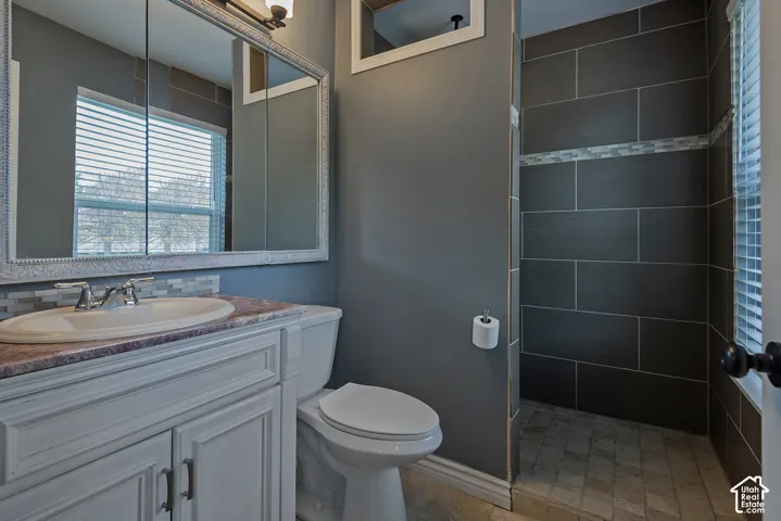 Bathroom featuring a vanity with integrated sink, stone-surface countertop, large wall-mounted mirror, tiled shower surround, and mosaic tile backsplash