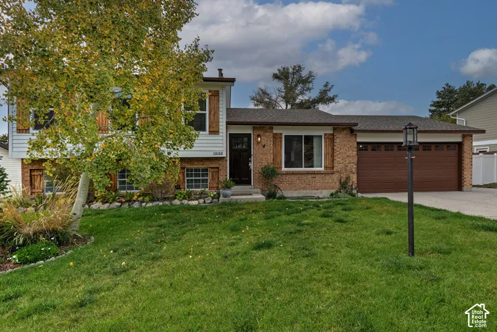 Split-level exterior featuring a combination of brick and horizontal siding, wood-toned shutters, an attached garage, and a manicured front lawn