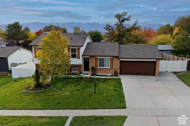 Multi-level exterior featuring brick masonry siding, dual-tone roof shingles, a wide attached garage, and a manicured front lawn with mature landscaping