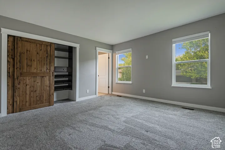 Room featuring neutral-toned carpeting, two dual-pane windows, and a sliding barn-style door with built-in storage shelving