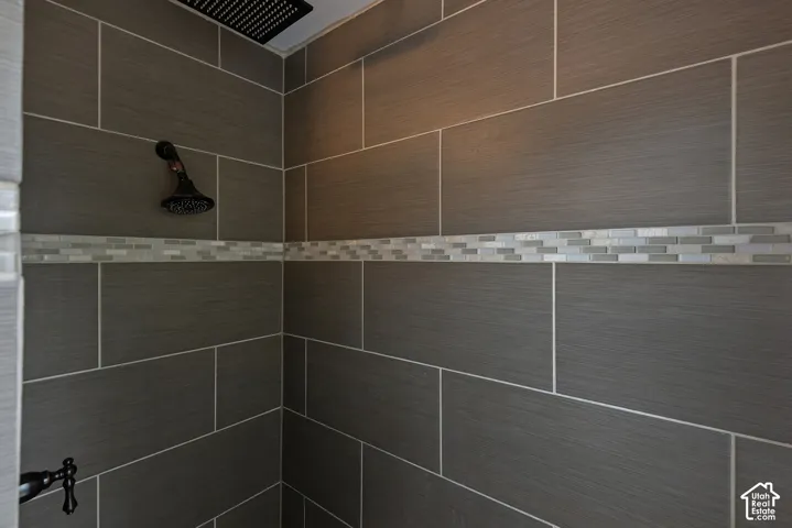 Shower enclosure featuring large-format rectangular wall tile, a decorative mosaic tile inlay, a ceiling-mounted rainfall showerhead, and a wall-mounted shower fixture in a matte finish
