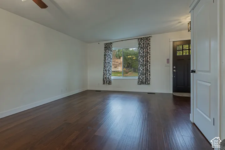 Wood-finish flooring, dark-toned exterior door with a windowed panel, ceiling fan, and large picture window
