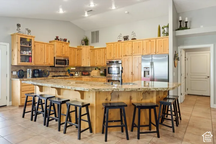Kitchen featuring natural wood cabinetry, stone countertops, stainless steel double wall ovens, a stainless steel refrigerator, and ceramic tile flooring