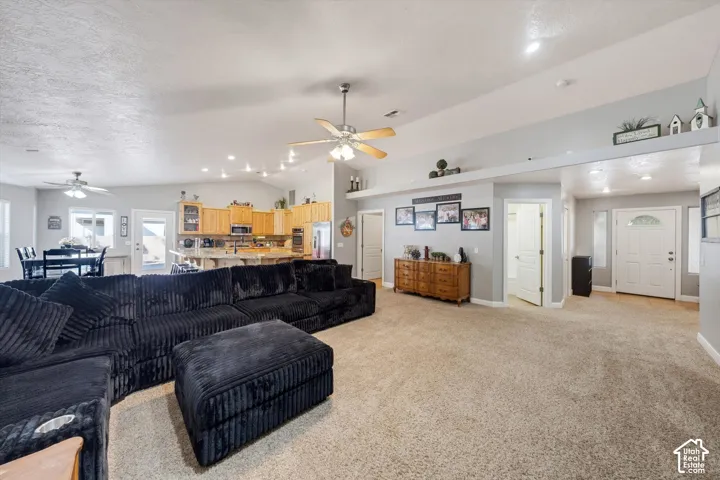 Open-concept interior featuring vaulted ceilings, recessed lighting, ceiling fans, built-in display shelving, and cabinetry with stone-surface countertops