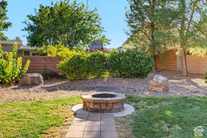 Outdoor space featuring a stone-block fire pit, paved stone walkway, manicured lawn, decorative boulder accents, and mature landscaping enclosed by a masonry wall