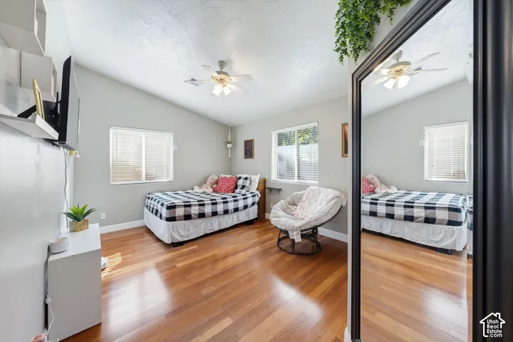 Room featuring wood-finish flooring, vaulted ceilings, dual-pane windows with blinds, and a ceiling fan