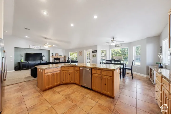 Open-concept kitchen featuring an expansive island with stone countertops, stainless steel dishwasher, wood cabinetry, tile flooring, and recessed ceiling lighting