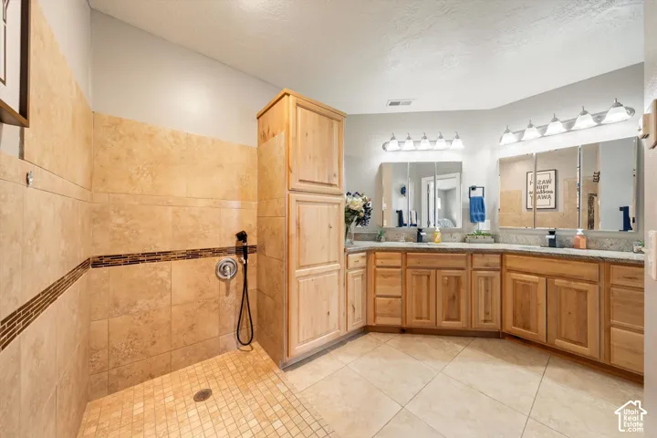 Natural wood cabinetry, stone-tile wall finishes with decorative inlay, large-format floor tiling, dual-sink vanity with stone countertop, and glass-front medicine cabinets