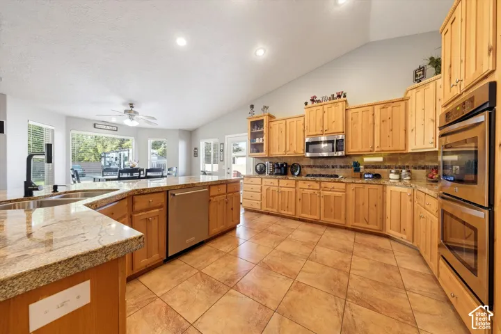 Kitchen featuring vaulted ceilings, stone-finish countertops, tile flooring, natural wood cabinetry, and built-in double ovens