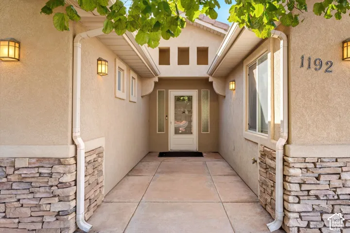 Stucco exterior entry featuring natural stacked stone veneer, concrete paver walkway, door with dual sidelights, and recessed exterior wall lighting