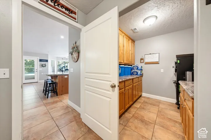Utility space featuring wood cabinetry, stone-finish countertops, ceramic tile flooring, and ceiling-mounted lighting