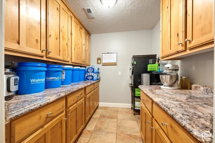 Custom natural wood cabinetry featuring extensive upper and lower storage, complemented by stone-patterned laminate countertops and tile flooring