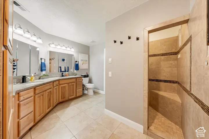 Bathroom featuring natural wood cabinetry, stone-finish countertops, dual mirrors with integrated lighting, tile flooring, and a walk-in shower with stone tile surround and built-in bench seating
