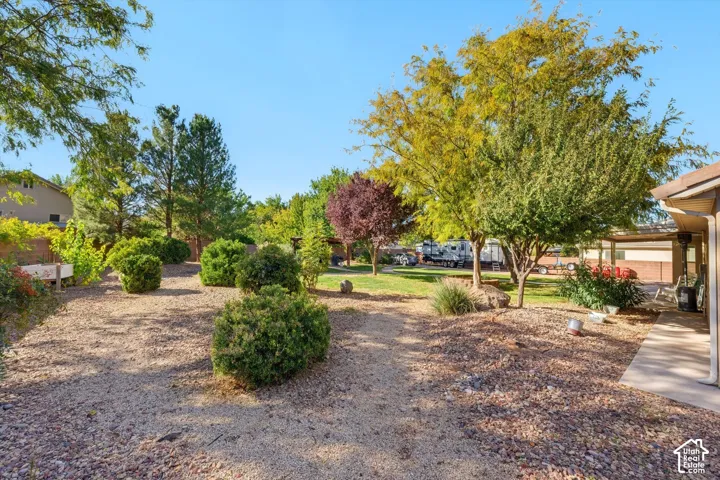Rear yard featuring gravel hardscaping, mature deciduous trees, manicured shrubs, a concrete patio, and perimeter masonry wall