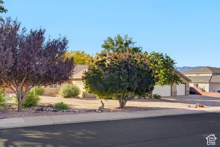 Exterior featuring a low-maintenance xeriscape front yard, stone-accented garage facade, concrete driveway, and mature landscaping