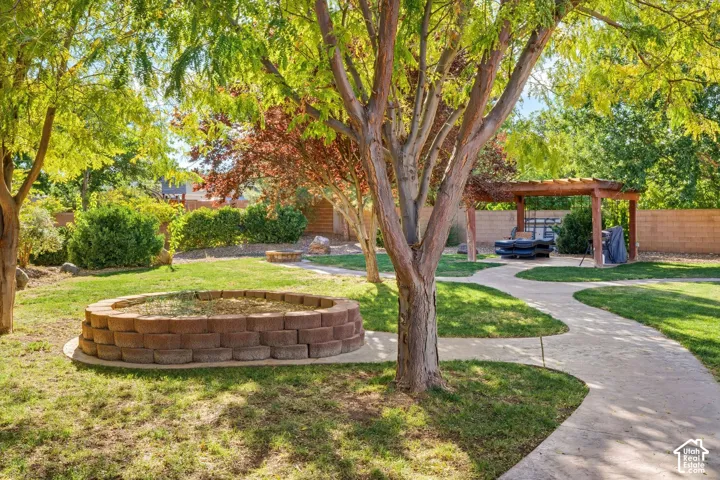 Landscaped backyard featuring a concrete pathway, tiered stone garden bed, pergola, and mature trees