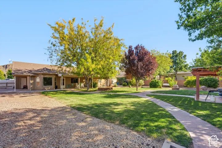 Expansive backyard featuring a sprawling lawn, mature trees, concrete pathways, a detached wooden pergola, and gravel landscaping