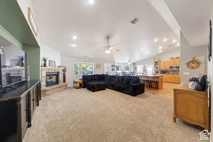 Vaulted ceilings, brick-surround fireplace with hearth, kitchen island with breakfast bar, built-in cabinetry, and recessed lighting
